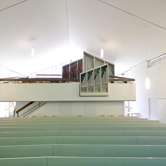Moderner Kirchenraum mit erhöhter Orgel und Bänken.