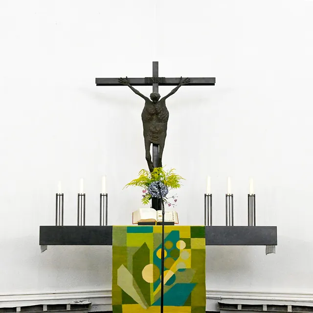 Moderner Altar mit Kruzifix, Kerzen und farbigem Textil.